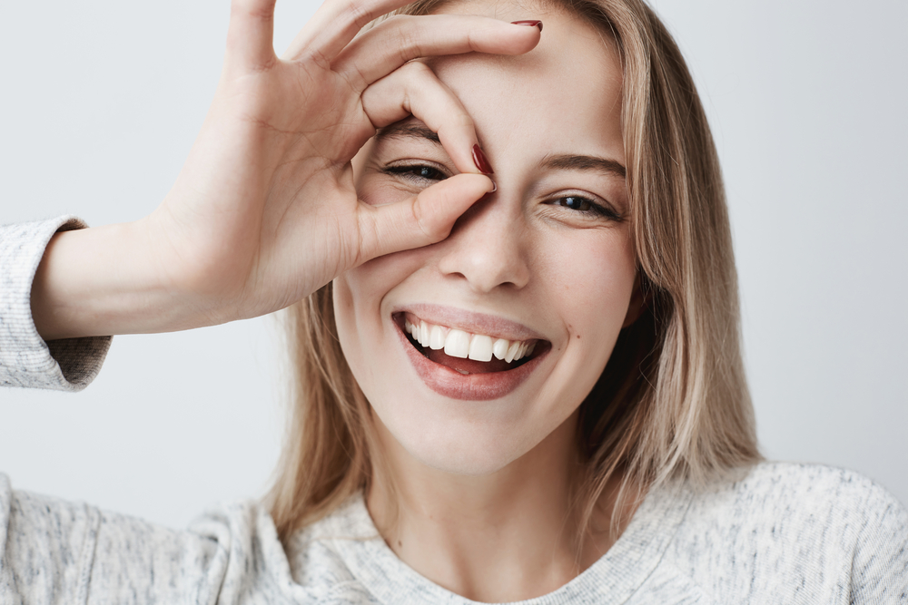 Happy woman smiling while making a circle around her eye with her fingers, symbolizing clear vision, comfort, and confidence with contact lenses – Contact Lenses Plymouth