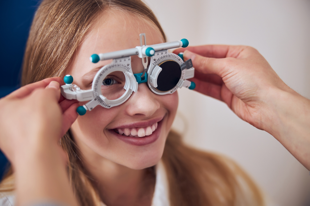 Smiling young woman wearing trial lens frames during an eye exam, representing accurate vision testing and a comfortable patient experience – eye exam plymouth