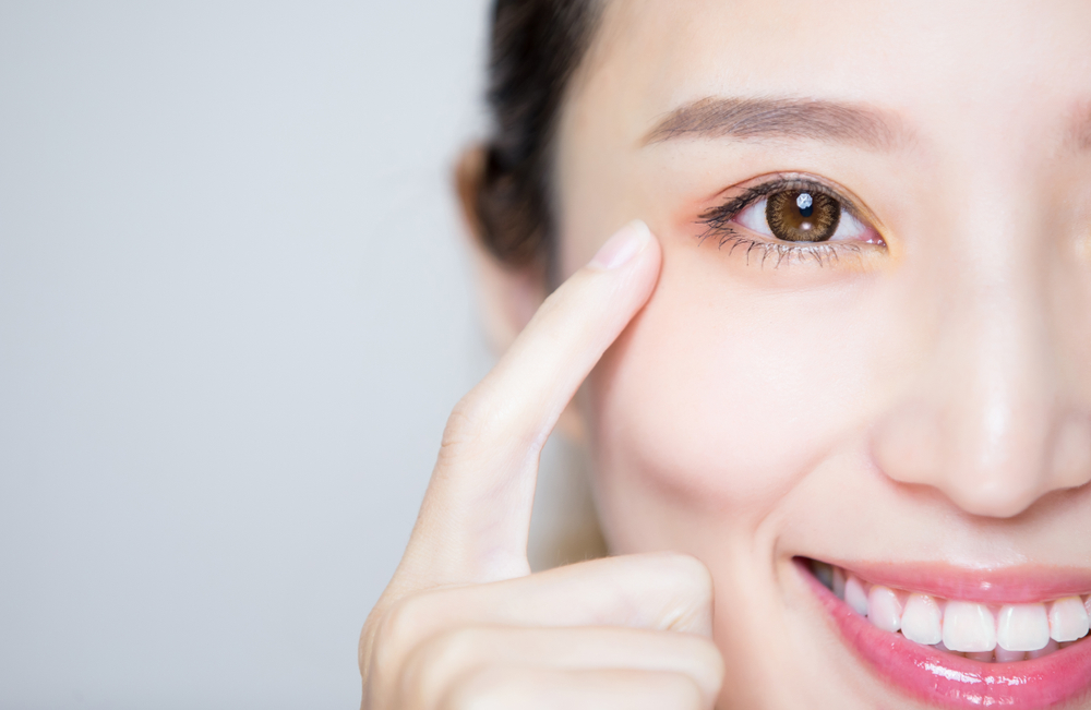 Close-up of a smiling woman pointing to her eye, representing eye health awareness, vision clarity, and the importance of regular eye exams – eye exam plymouth