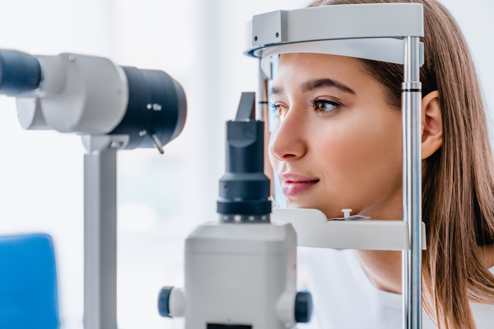 A young woman sits calmly as she undergoes an eye exam using a slit lamp at an optometry clinic, focusing intently on the device. - Kennedy Vision Health Center