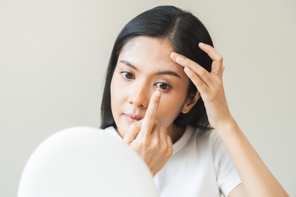 Woman carefully inserting a contact lens while looking into a mirror, representing proper contact lens use, comfort, and professional vision care – Contact Lenses Plymouth
